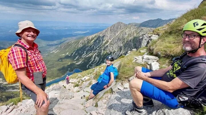 Rast mit Seeblick | © DAV Markt Schwaben | Foto Sabine Hainz Drei Wandernde sitzen auf Felsen oberhalb eines Bergsees; im Hintergrund steile Hänge, Wolken und weite Aussicht ins Tal. | © DAV Markt Schwaben | Foto Sabine Hainz