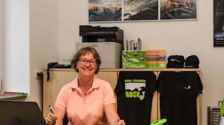 Geschäftsstelle | Anna Maria Blau | © DAV Markt Schwaben Blick in die Geschäftsstelle des Alpenvereins: Ein Mitarbeiter am Schreibtisch arbeitet am Laptop, während Broschüren, Vereinskleidung und Outdoor-Ausrüstung im Hintergrund präsentiert werden. Jetzt Kontakt aufnehmen und mehr über Mitgliedschaft und Angebote erfahren! | © DAV Markt Schwaben